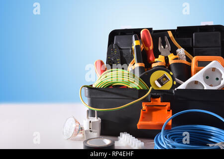 Toolbox full of tools and electrical equipment on white table and blue isolated background. Front view. Horizontal composition. Stock Photo