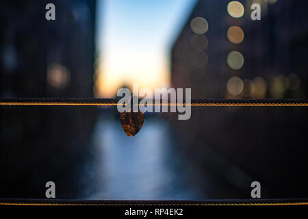 Love locks hang from a bridge. Red love lock or padlock with white heart on the bridge over the river. Valentine's Day. Love locks is a symbol of Stock Photo