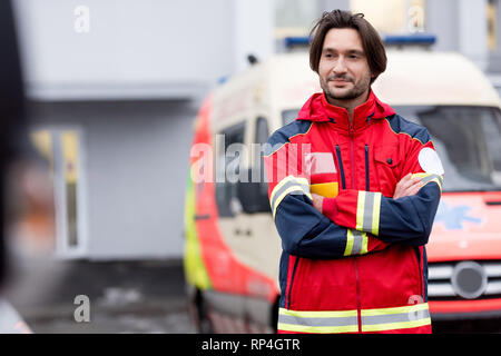 Confident paramedic in red uniform standing on street with crossed arms