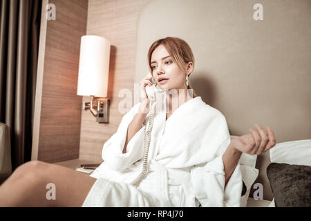 Blonde woman wearing nice earrings calling room service Stock Photo