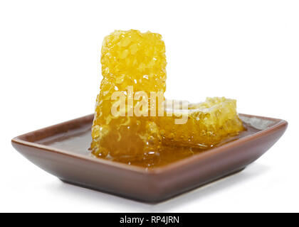 two pieces of golden organic honeycomb in a small dish isolated on a white background  with pouring honey, focus on the subject Stock Photo