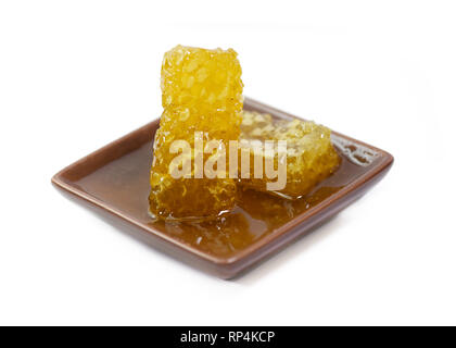 golden organic honeycomb in a small bowl isolated on a white background  with pouring honey, focus on the subject Stock Photo