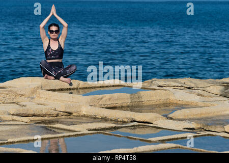 woman sitting on the limestone salt pans in malta, practicing yoga and meditating in the sun Stock Photo