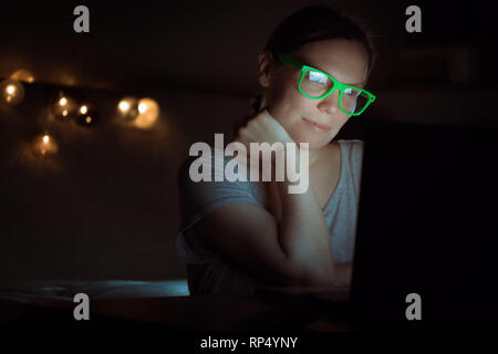 Woman working overtime on laptop computer late at night, low key portrait of female entrepreneur in home office environment finishing business task Stock Photo
