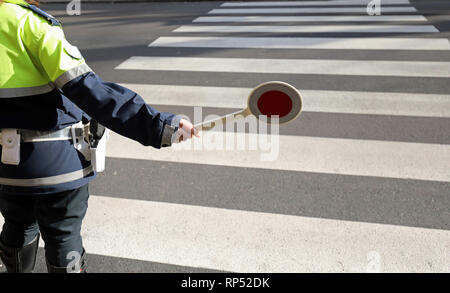 policeman stops the cars on the pedestrian crossing with the special pallet to regulate traffic Stock Photo