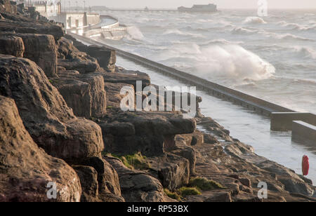 Waves crashing against the seawall in strong winds on north shore cliffs  with North Pier in background in January at Blackpool Lancashire England UK Stock Photo