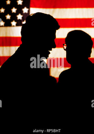 A silhouetted President Bill Clinton (left) talks with US Senator Sam Nunn (D-GA). Nunn is chairman of the powerful senate Armed Services Committee. A large American flag hangs in the background. Stock Photo