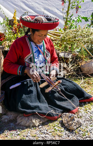 Woman in traditional dress sits and weaves alpaca yarn in Sacred Valley, Cusco Region, Peru. Stock Photo