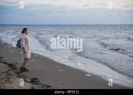 Woman in coat walking on the seashore. Stock Photo