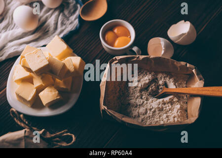 Top view of diced butter, sack of flour, raw yolks and egg shells on brown wooden table. Ingredients for baking homemade pie. Stock Photo