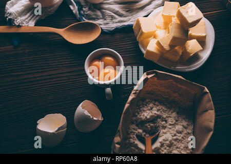 Top view of butter, sack of flour, raw yolks and egg shells on brown wooden table. Ingredients for baking homemade pie. Stock Photo
