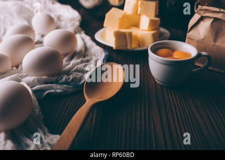 Close-up of ingredients for cooking pie on dark brown wooden table. Diced butter, raw eggs, yolks, flour,  ready for making homemade bakery. Stock Photo