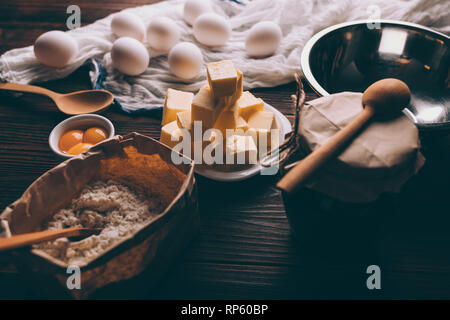 Close-up of ingredients and utensils for cooking pie on dark wooden table. Raw eggs, yolks, flour, butter and an empty bowl ready for making homemade  Stock Photo