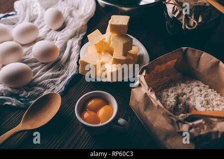 Close-up of ingredients for cooking pie on dark wooden table. Diced butter, raw eggs, yolks, flour,  ready for making homemade bakery. Stock Photo
