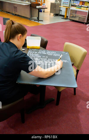 A young woman in a popular Garden Centre Café in North Yorkshire, writing out the Chef’s Special Lunch time menu for display on a blackboard. Stock Photo
