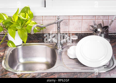 The Clean dishes are drying, on rustic kitchen metal sink . Stock Photo