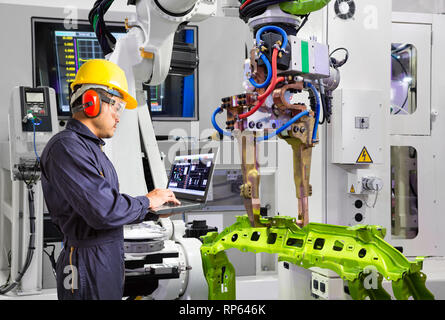 Maintenance engineer using laptop computer control robot grip automotive workpiece in smart factory, Industry 4.0 concept Stock Photo