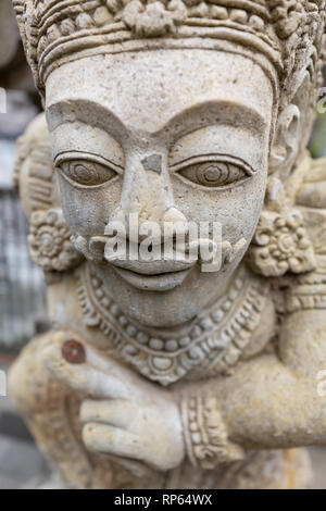 Closeup of face of stone carved statue of a god on wall of Hindu temple in Bali Stock Photo