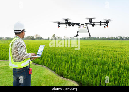 Technician farmer use wifi computer control agriculture drone fly to sprayed fertilizer on the rice fields, Smart farm 4.0 concept Stock Photo