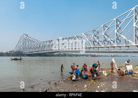 Howrah Bridge - Popularly known as the Rabindra Setu overlooking the Mullick Ghat with local people bathing washing on a sunny day and blue sky. Stock Photo