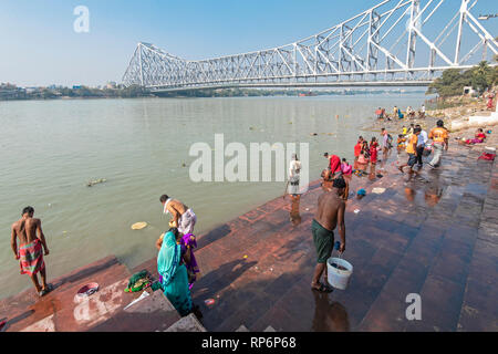 Howrah Bridge - Popularly known as the Rabindra Setu overlooking the Mullick Ghat with local people bathing washing on a sunny day and blue sky. Stock Photo