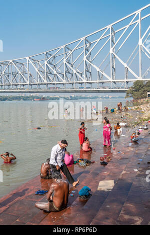 Howrah Bridge - Popularly known as the Rabindra Setu overlooking the Mullick Ghat with local people bathing washing on a sunny day and blue sky. Stock Photo