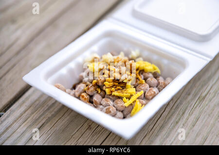 Asian Japanese natto fermented soy dish meal closeup in container Japan box and toppings soy sauce garlic and ginger on wooden table macro Stock Photo