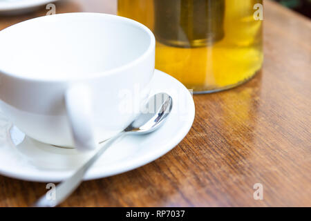 Closeup of one white cup on plates and green or oolong tea in breakfast brunch cafe restaurant wooden table with spoon and teapot or pot Stock Photo