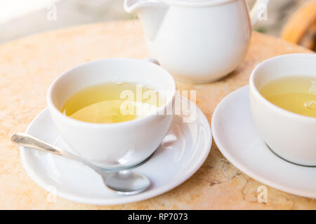 Closeup of two white cups on plates saucers of green or oolong tea in breakfast brunch outdoor cafe restaurant outside table with teapot pot Stock Photo