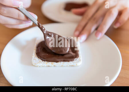 Closeup of rice cake with woman hand spreading chocolate hazelnut spread with spoon sauce or syrup brown vegan vegetarian snack dessert one single pie Stock Photo