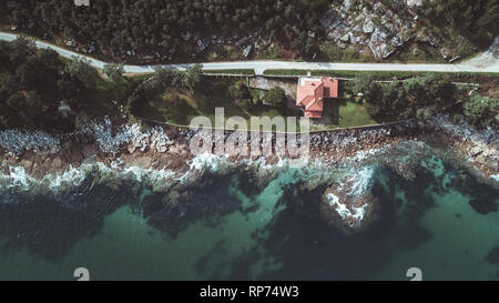 Drone aerial view of remote residential house on rocky beach in Galicia on a sunny bright day. Stock Photo