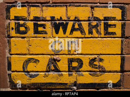 Beware of Cars sign painted on yellow on an old red brick wall. Stock Photo