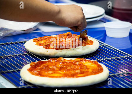 chef making pizza at kitchen, Chef spreading cheese toppings on pizza base Stock Photo