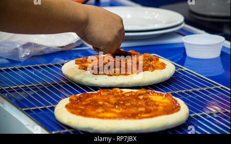 chef making pizza at kitchen, Chef spreading cheese toppings on pizza base Stock Photo