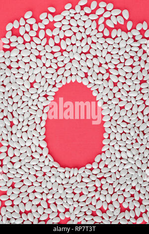 Easter background, Easter egg shape surrounded by a white candy coated sunflower seeds on a coral colored background Stock Photo