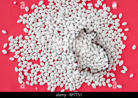 Plentiful pile of white candy coated sunflower seeds with a rabbit shaped cookie cutter on a coral colored background Stock Photo