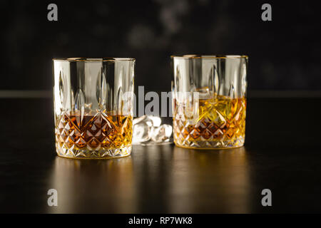 whiskey in two glasses, stand on a dark table and in the background next to the lying ice Stock Photo