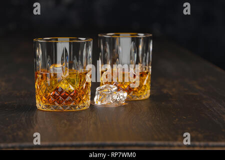 whiskey two glasses with ice, stand on a dark old wooden table on a black background Stock Photo