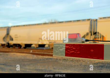 Close-up of the end tip of a railway boom barrier at a level railway crossing with a train passing by in the background; Bryan, Texas, USA. Stock Photo