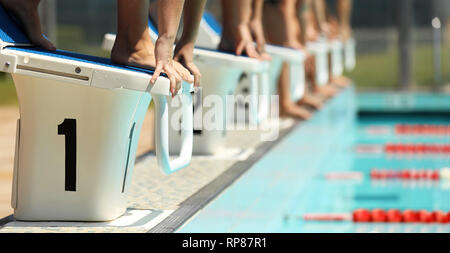 A line up of swimmers preparing to jump of the starting blocks in a swimming competition. Diving blocks focus on hand and feet lane 1. Stock Photo