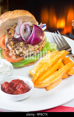 Homemade Quorn burger in a sourdough bun with lettuce, tomato, red onion, Sweet potato chips/fries, and served with ketchup and soy yogurt dips. Stock Photo