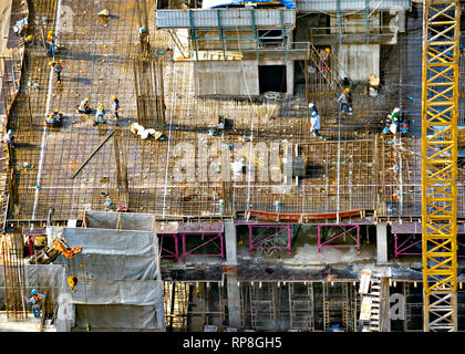 Aerial view of a building construction with tower crane, scaffolding, formwork, equipment, and work crews placing reinforcing steel bars. Stock Photo