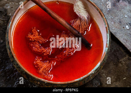 Alpaca yarn is dyed red in bowl with cactus paddle in Sacred Valley, Cusco Region, Peru. Stock Photo