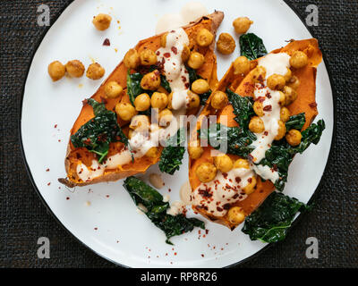 Baked sweet potatoes loaded with spicy chickpeas and kale and a tahini Dressing. Stock Photo