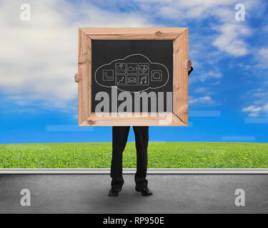 Man holding blackboard with hand-drawn cloud app icons on concrete floor and natural sky grass background Stock Photo
