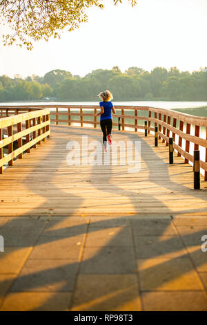 Photo from back of sports woman running on wooden bridge on summer. Stock Photo