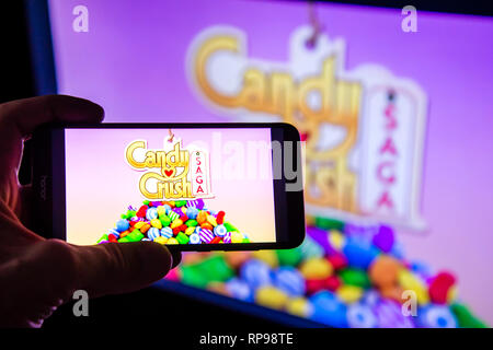 Los Angeles, California, USA - 21 February 2019: Hands holding a smartphone with CANDY CRUSH SAGA game against the big screen. Stock Photo