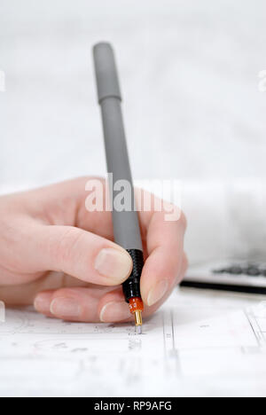 Woman's hand holding rapidograph, architectural plans in background Stock Photo