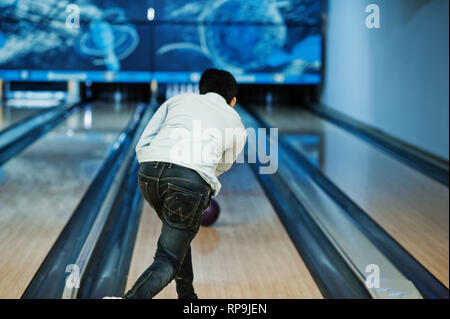 Back of asian man in jeans shirt standing at bowling alley with ball on hands and throw it. Stock Photo