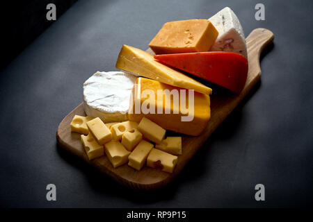 Wooden board with different kinds of cheeses on black smooth table